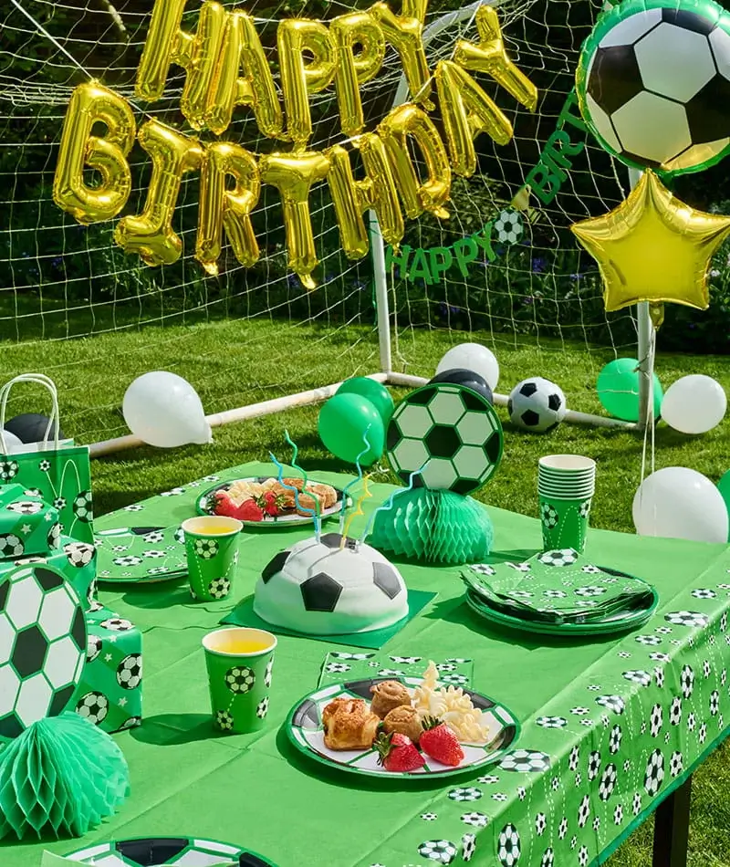 Football-themed birthday party table with a football-shaped cake, football-print tableware, balloons, gift bags, and a Happy Birthday balloon banner.